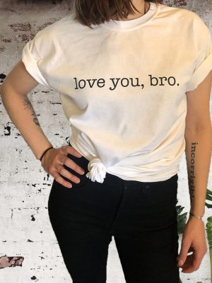 Woman wearing The Barton Brothers white 'love you, bro' t-shirt in front of a painted brick wall